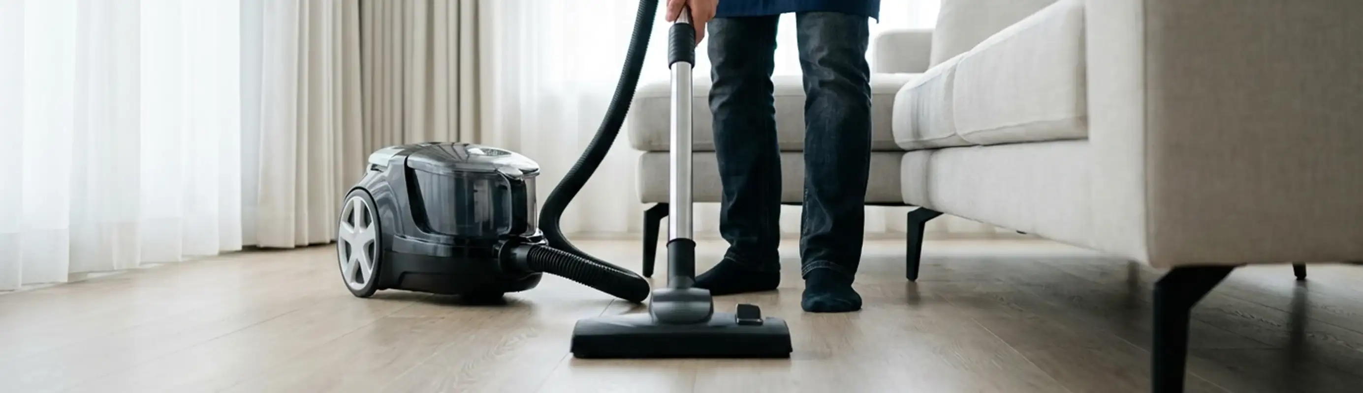 Professional house cleaner vacuuming a living room floor with a canister vacuum cleaner, Charleston, SC.