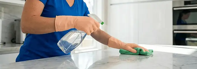 Maid service worker spraying and wiping a kitchen countertop with a microfiber cloth for sanitizing, Charleston, SC.