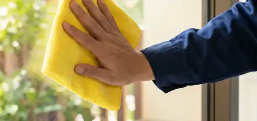 House cleaner wiping a glass window with a yellow microfiber cloth for streak-free cleaning, Charleston, SC.